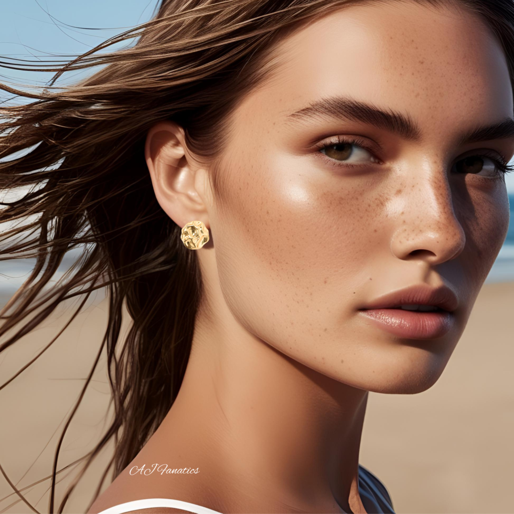 Organic Modern Free-Spirited Ripples Statement Earrings in gold-plated stainless steel, styled on a model with windswept hair at the beach.